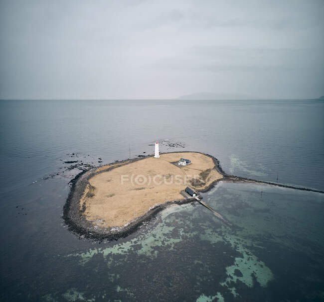 Drone vista de pequena ilha com farol branco perto da casa e galpão localizado no meio do mar no dia maçante na Islândia — Fotografia de Stock
