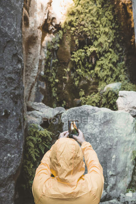 Rückansicht des Wanderers neben großer roter Steinhöhle beim Fotografieren mit dem Smartphone — Stockfoto