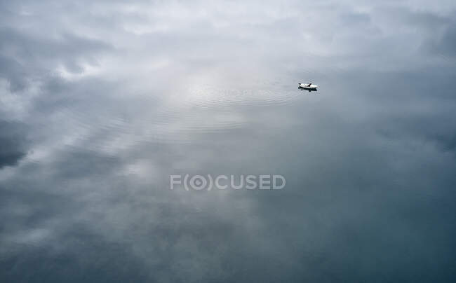 Grand angle de navire blanc lointain flottant sur l'eau réfléchissante d'un lac paisible par temps nuageux — Photo de stock