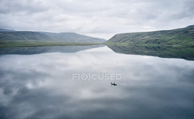 Drohnen-Ansicht eines entfernten Bootes, das an einem trüben Tag in Island auf ruhigem, reflektierendem Wasser des sauberen Sees schwimmt — Stockfoto