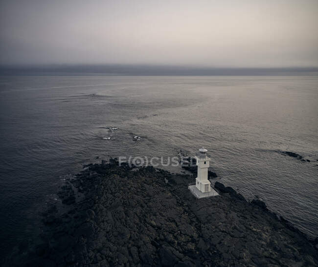 Drone view of white lighthouse located on rocky coast near waving sea in stormy morning in Iceland — Stock Photo