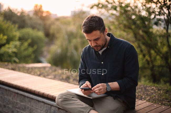 Empresário usando telefone inteligente enquanto sentado no banco no parque — Fotografia de Stock