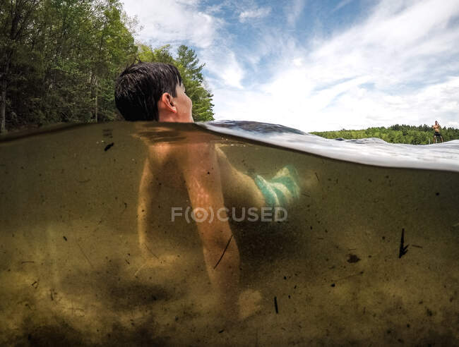 Розділений вид на воду хлопчика в озері в теплий літній день . — стокове фото