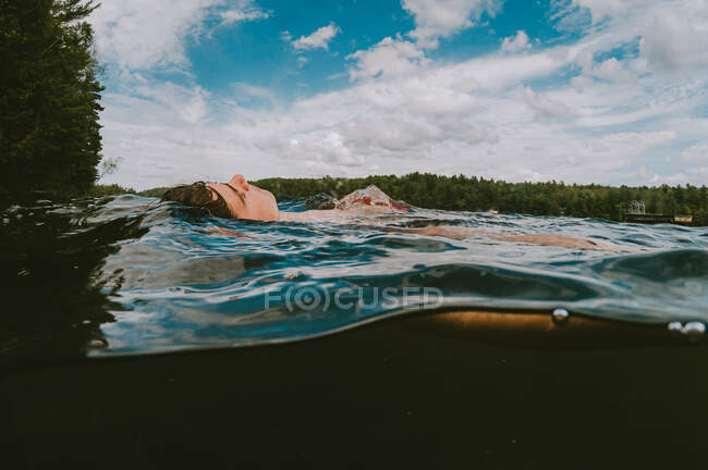 Split water view of boy floating in a lake on a warm summer day. — Stock Photo