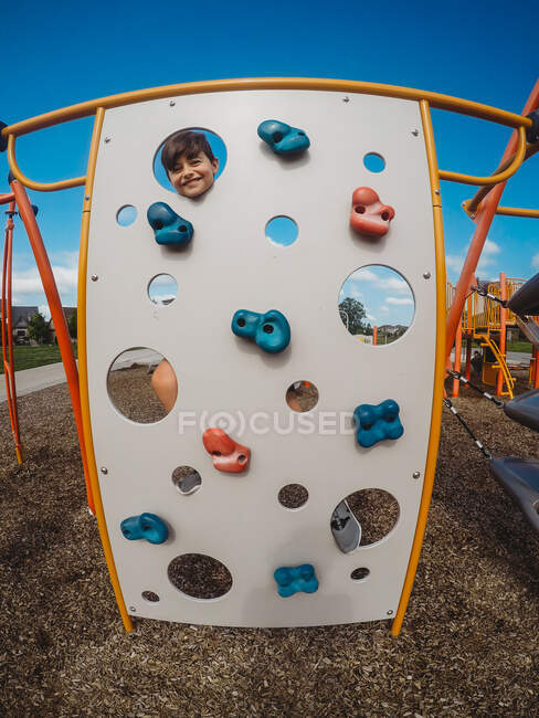 Glücklicher Junge blickt auf Spielplatz durch Löcher in Kletterer. — Stockfoto