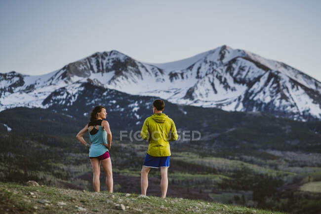 Two friends catch their breath while running in front of large peak — Stock Photo