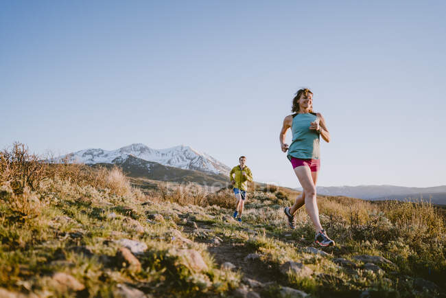 Una mujer y un hombre corren por las montañas durante la hora dorada - foto de stock