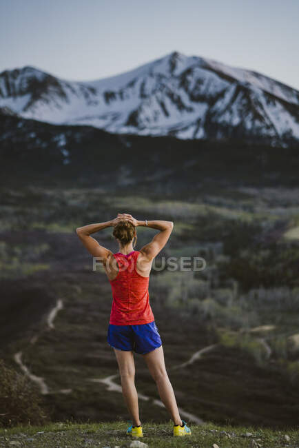 A strong female runner stands on a summit taking in the mountain view — Stock Photo