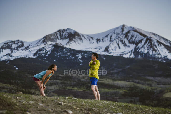 Двоє друзів розтягуються разом перед стежкою, що біжить у горах — стокове фото