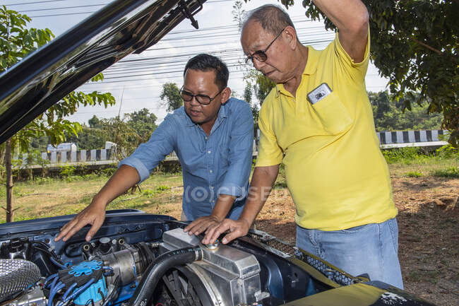 Two men looking under the hood of American muscle car in Thailand — Stock Photo