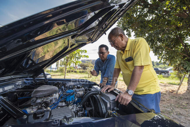 Two men looking under the hood of American muscle car in Thailand — Stock Photo
