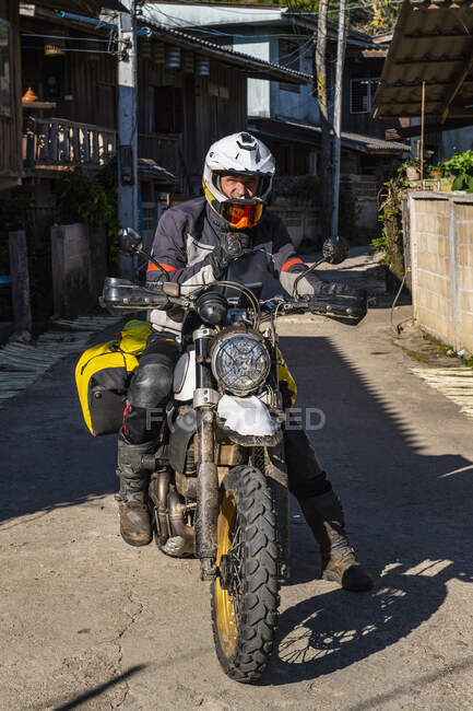 Homem parando na estrada com sua motocicleta na aldeia tailandesa — Fotografia de Stock