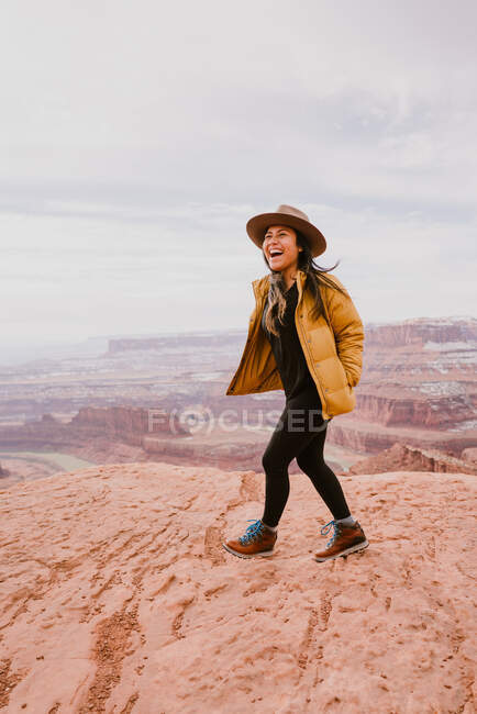Una donna con il cappello a tesa ride mentre cammina sopra il canyon del deserto — Foto stock