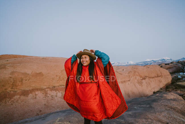 A woman wearing brimmed hat and puffy poncho hiking in the desert — Stock Photo