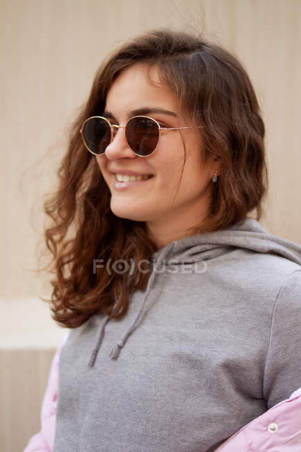 Eine junge Frau mit Sonnenbrille und Kapuzenpulli schaut zur Seite und lächelt. — Stockfoto