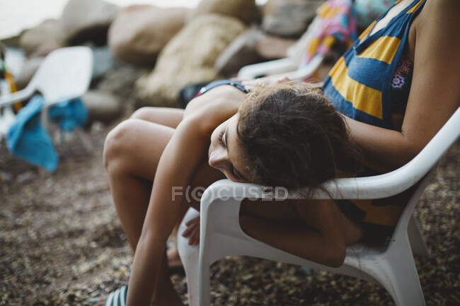 Ein junges Mädchen ruht sich am Strand auf den Schenkeln ihrer Mutter aus — Stockfoto