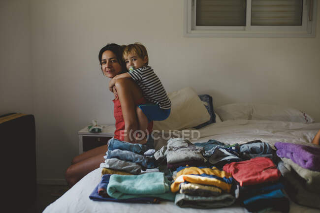 Madre e hijo divirtiéndose cerca de una pila de ropa doblada - foto de stock
