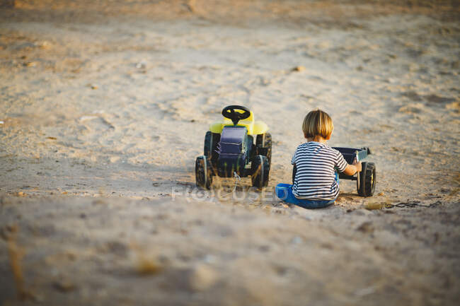 Young boy playing with toy trucks in the desert — Stock Photo