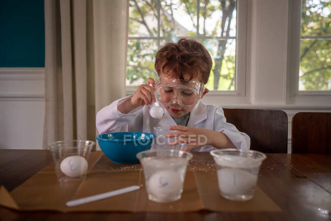 Joven científico concentrado en un experimento con bata de laboratorio - foto de stock