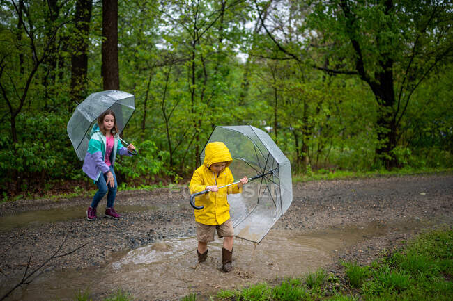 Ragazzo e ragazza che giocano sotto la pioggia con gli ombrelli — Foto stock