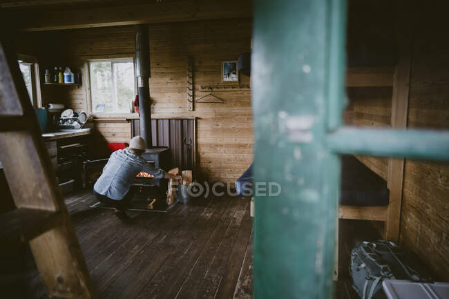 Вид через дверний проріз жінки, що закидає вогонь всередині сільської кабіни — стокове фото
