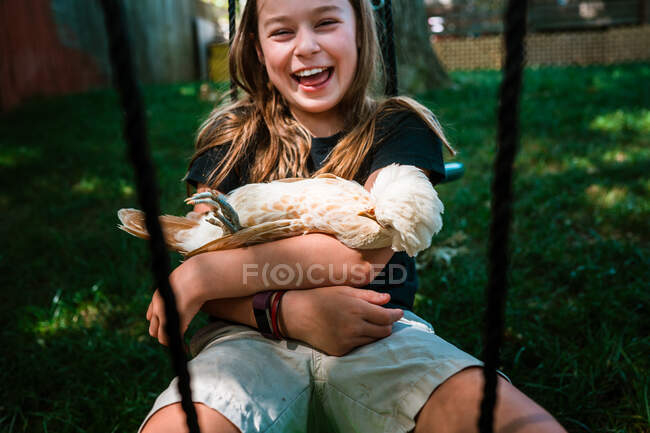 Young girl laughing while swinging with her pet chicken — Stock Photo