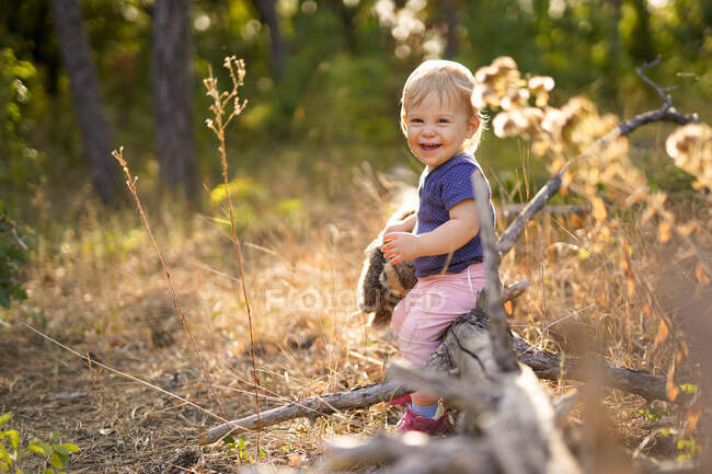 Bambino piccolo che ride e si siede su un albero caduto — Foto stock