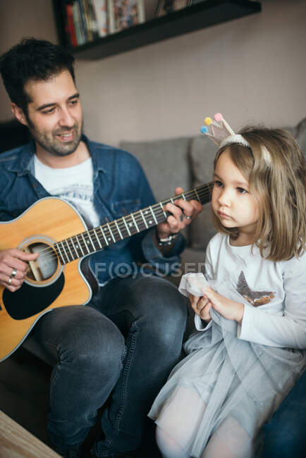 Un padre tocando la guitarra a su hija. - foto de stock