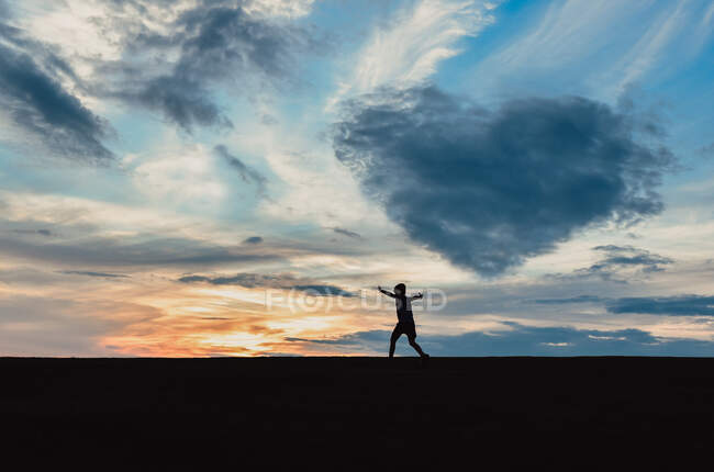 Silhouette d'enfant contre le ciel au coucher du soleil avec un nuage en forme de coeur. — Photo de stock