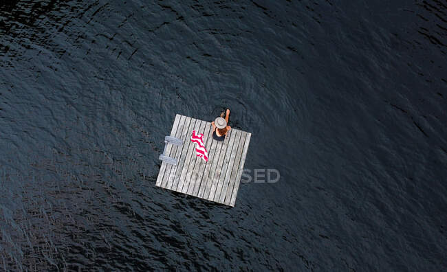 Aérea de mujer relajándose sola en muelle flotante en el lago en verano. - foto de stock