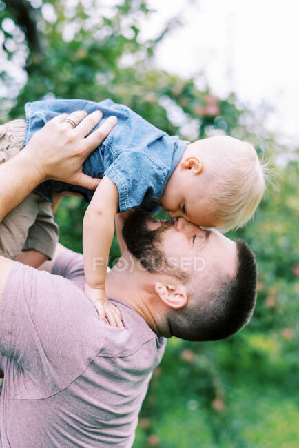 Un padre joven y su hijo acurrucándose afuera - foto de stock