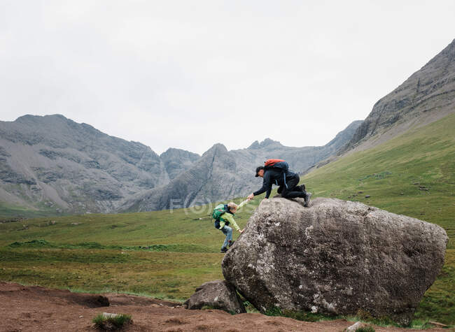 Отец помогает сыну взобраться на скалу на острове Скай, Шотландия — стоковое фото