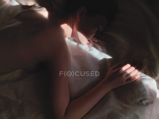 Оголена жінка лежачи на білому ліжку в смузі сонячного світла — стокове фото