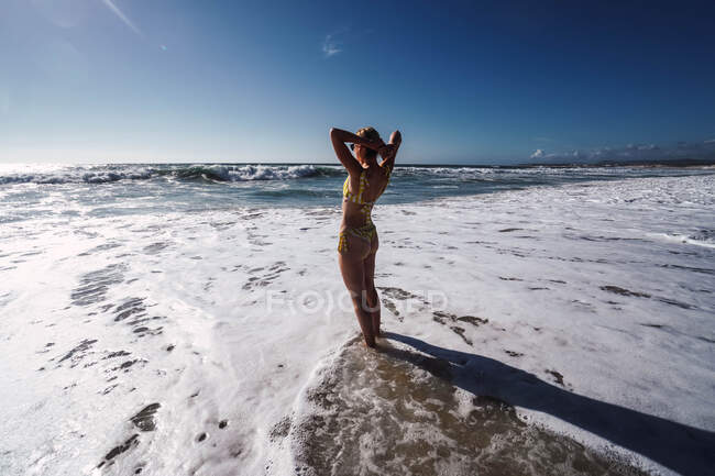 Frau im Badeanzug am Strand mit Wellen und Schaum am Strand — Stockfoto