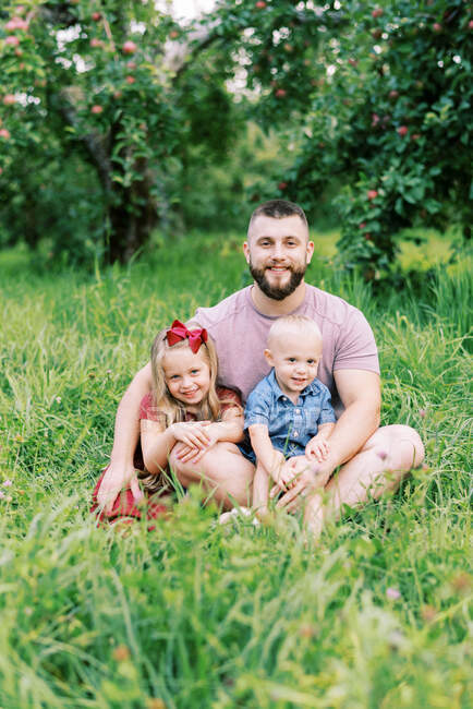 Отец с двумя детьми, сидящими в траве снаружи — стоковое фото