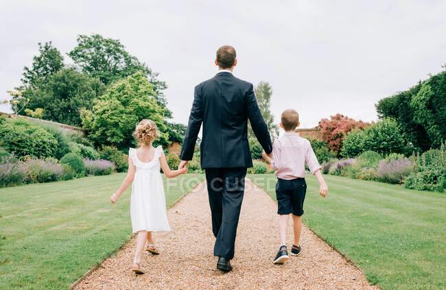 Pai e filhos vestidos para um casamento andando em um belo jardim — Fotografia de Stock