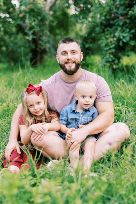Vater sitzt mit seinen beiden Kindern im Gras — Stockfoto