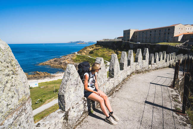 Pilgrim woman sitting on the wall of a castle against the sea — Stock Photo