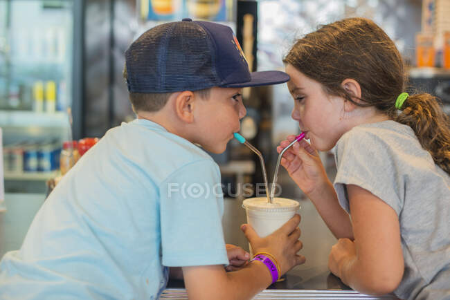 Gêmeos compartilhando um milkshake em um restaurante — Fotografia de Stock