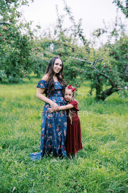Uma jovem mãe e sua filha envelhecida no jardim de infância em um pomar — Fotografia de Stock