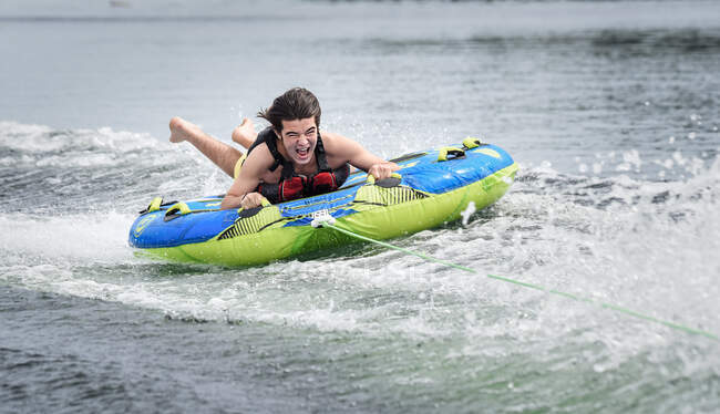 Adolescent excité s'amuser sur un tube tiré par un bateau sur un lac. — Photo de stock