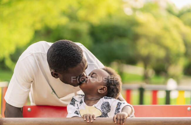 Padre besando a su hija pequeña en los juegos del parque - foto de stock