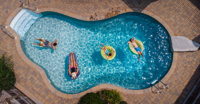 Vista aérea de la familia flotando en una piscina en el día de verano. - foto de stock