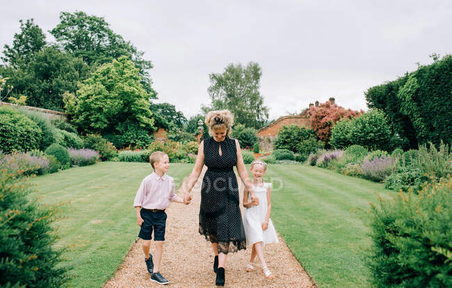 Mère et ses enfants à un mariage marchant dans un beau jardin — Photo de stock