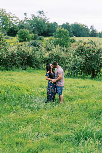 Man and woman sharing a kiss in a meadow among apple trees — Stock Photo