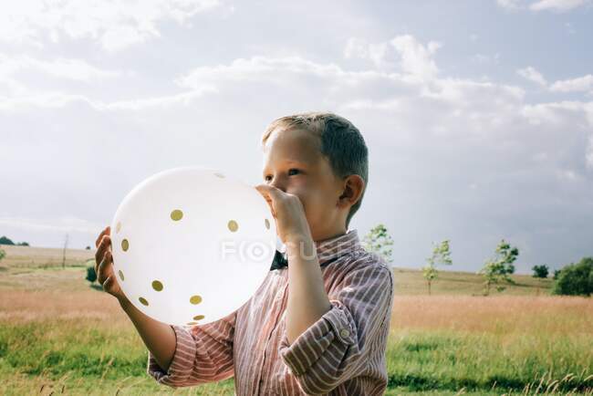 Boy in shirt and bow tie blowing up a wedding balloon — Stock Photo