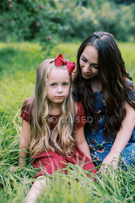 Una niña de cinco años y su joven madre sentadas en la hierba - foto de stock