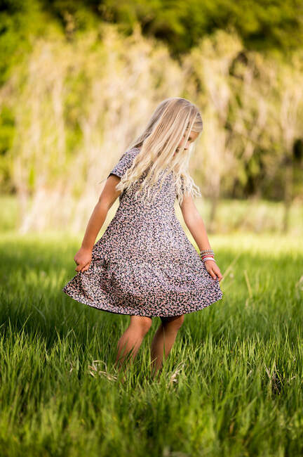 Blonde fille tourbillonnant une robe dans un champ d'herbe verte — Photo de stock
