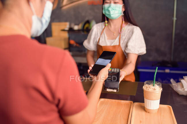 Жінка тримає смартфон близько до електронної платіжної машини — стокове фото