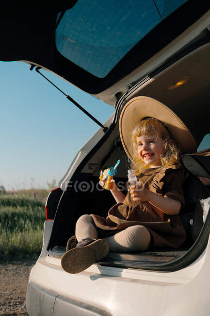 Маленька дівчинка сидить у багажнику автомобіля з мильними бульбашками — стокове фото